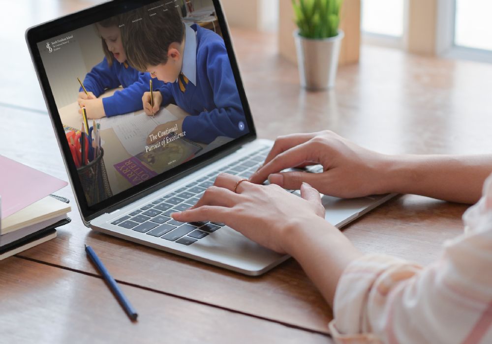 South Farnham homepage on laptop, woman typing on keyboard in a light blouse.