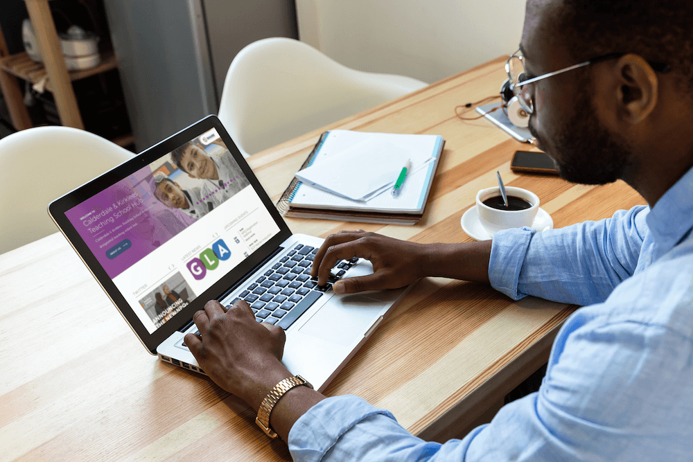 Man looking at CKTSH website on a laptop on a wooden table next to a black coffee